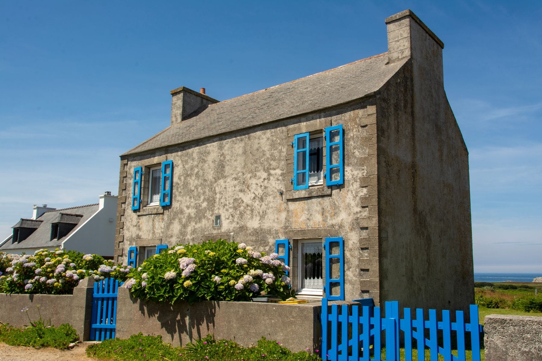 Maison bretonne en pierre aux volets bleus ouverts et jardin fleuri